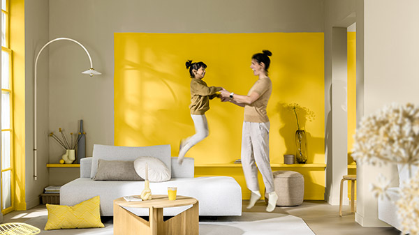 Mãe e filha brincando numa sala de estar moderna. Atrás delas está uma parede de destaque pintada de amarelo.